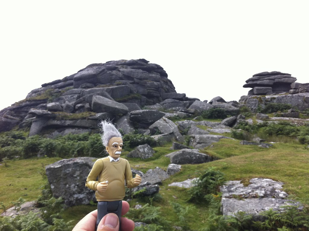 Einstein figure held up in front of dramatic granite tor outcrop on Dartmoor