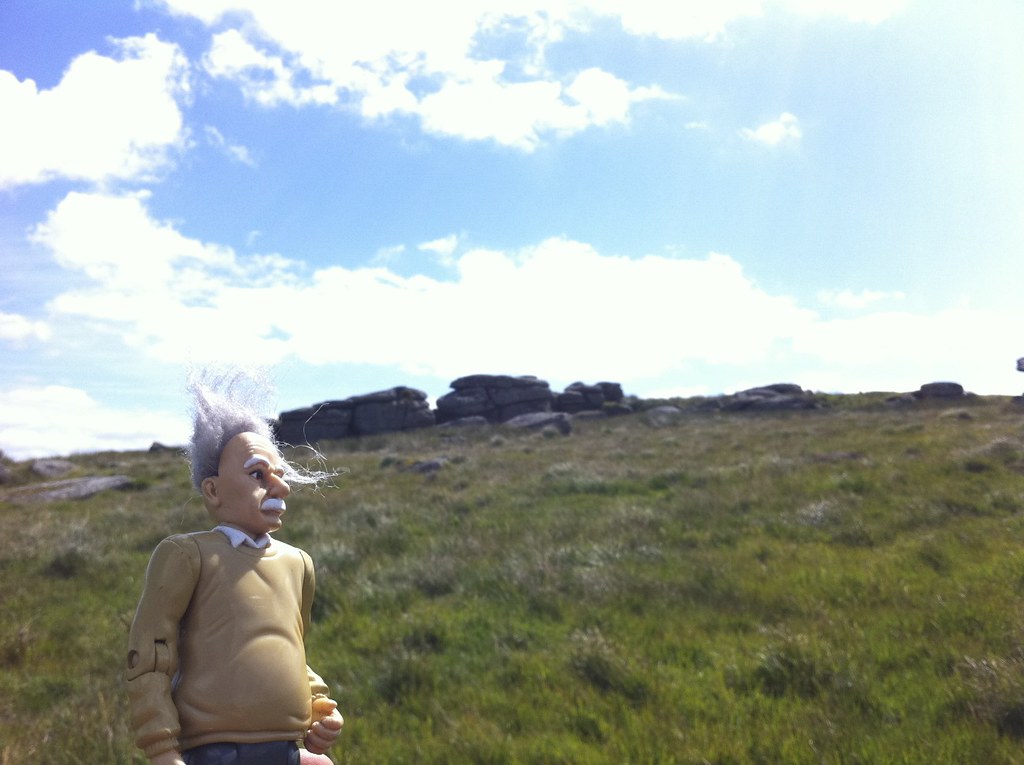 Einstein figure gazing up at a Dartmoor tor under a bright blue sky